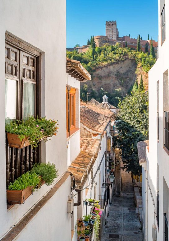 White facades decorated with pots and the mountain crowned with the Alhambra as a panorama of our visit to the typical neighbourhoods of Granada.