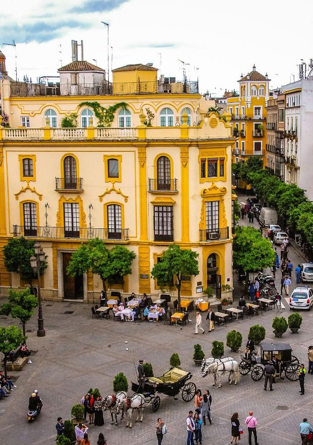 Building of traditional Sevillian architecture with its horse carriages touring the square.